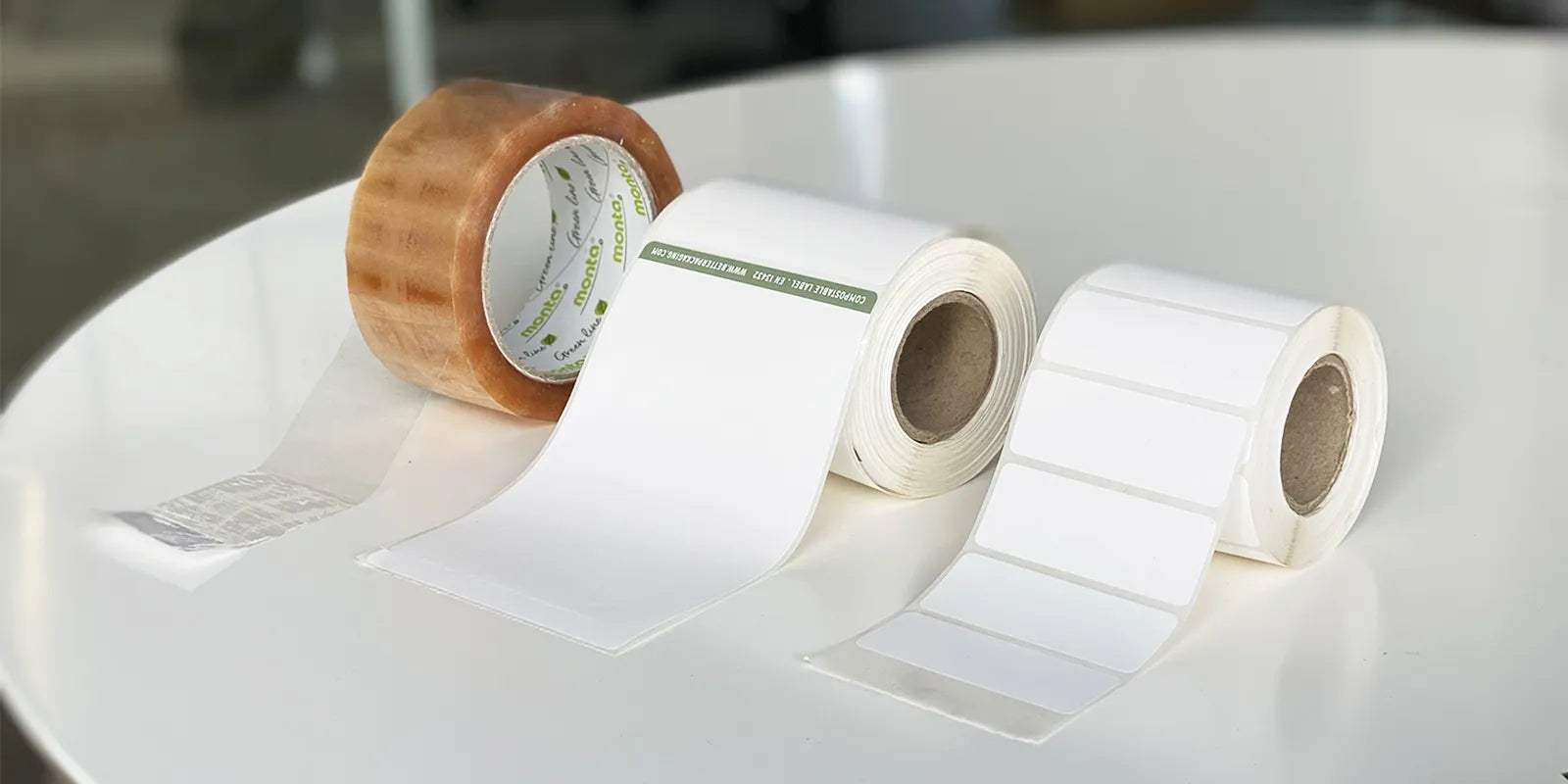 Two rolls of white label paper on a white surface with a blurred background